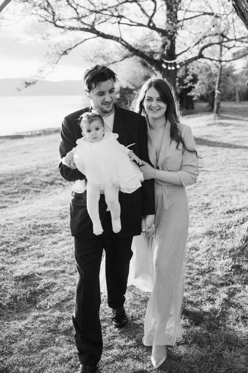 Battesimo Roma — famiglia in passeggiata sotto un albero con vista sul lago, scatto reportage in bianco e nero