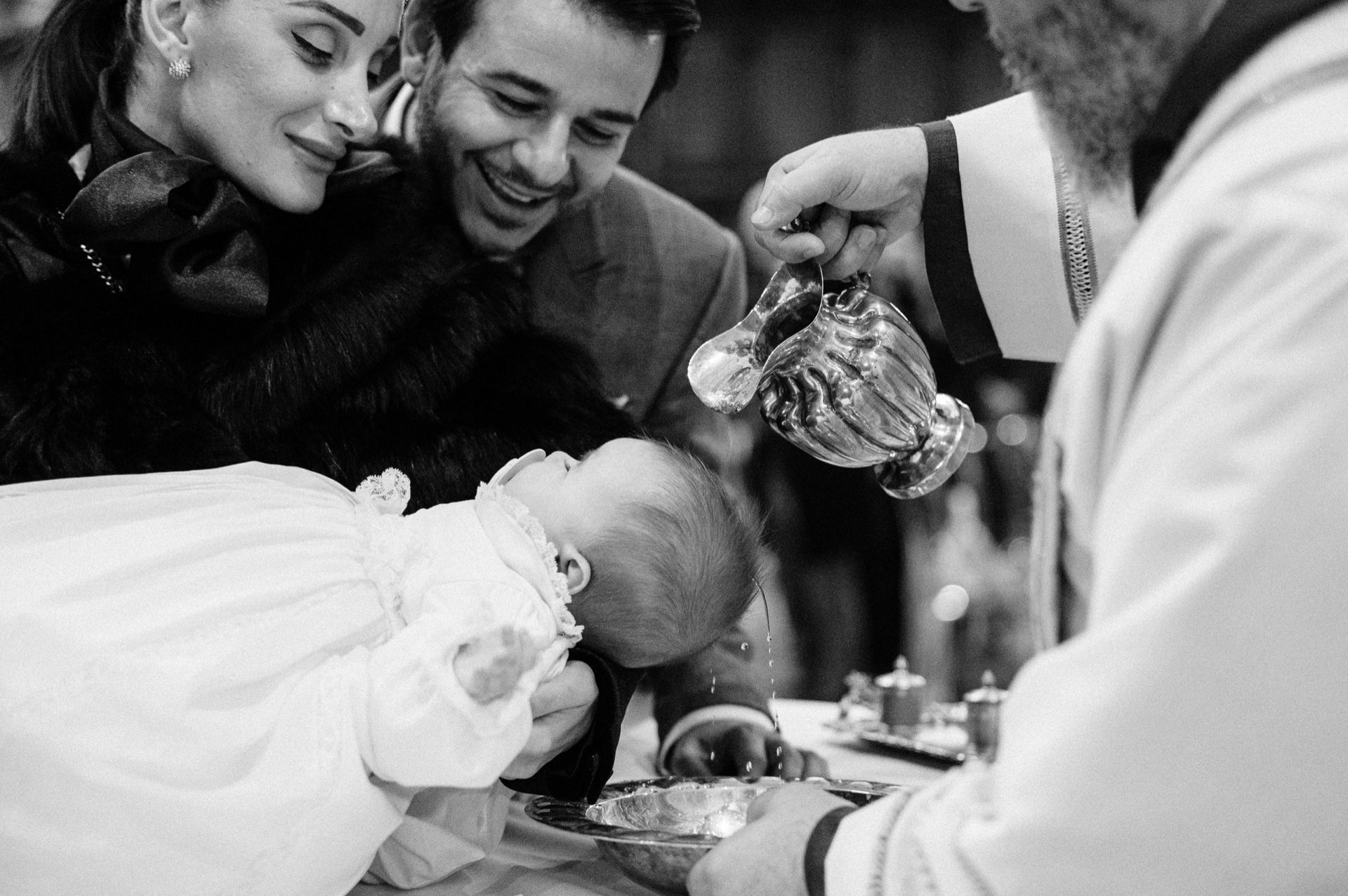 Fotografo battesimo Roma — momento del rito in chiesa, il sacerdote versa l'acqua benedetta sulla bambina tra le braccia dei genitori