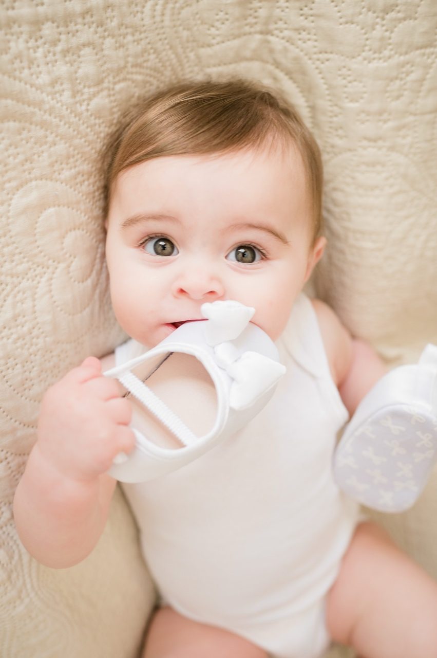 Preparativi battesimo Roma — bambina mordicchia la scarpetta bianca da battesimo