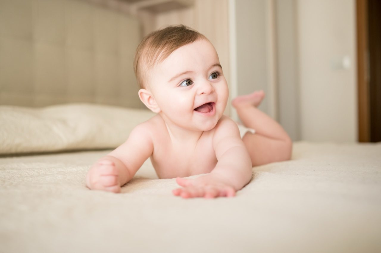 Preparativi battesimo Roma — bambina sorride sul letto durante la sessione fotografica