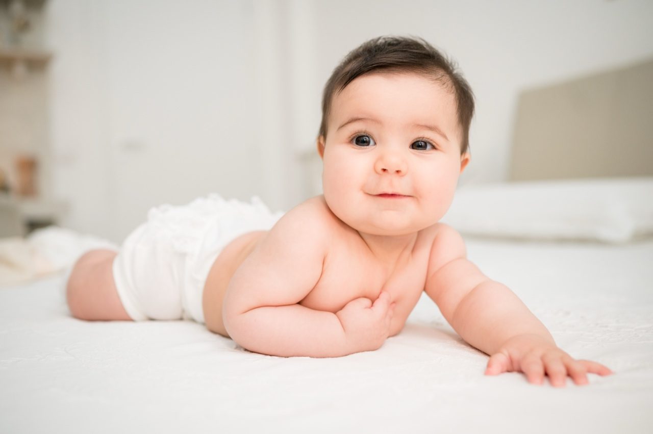 Preparativi battesimo Roma — bambina sorride sul letto bianco durante i preparativi della cerimonia