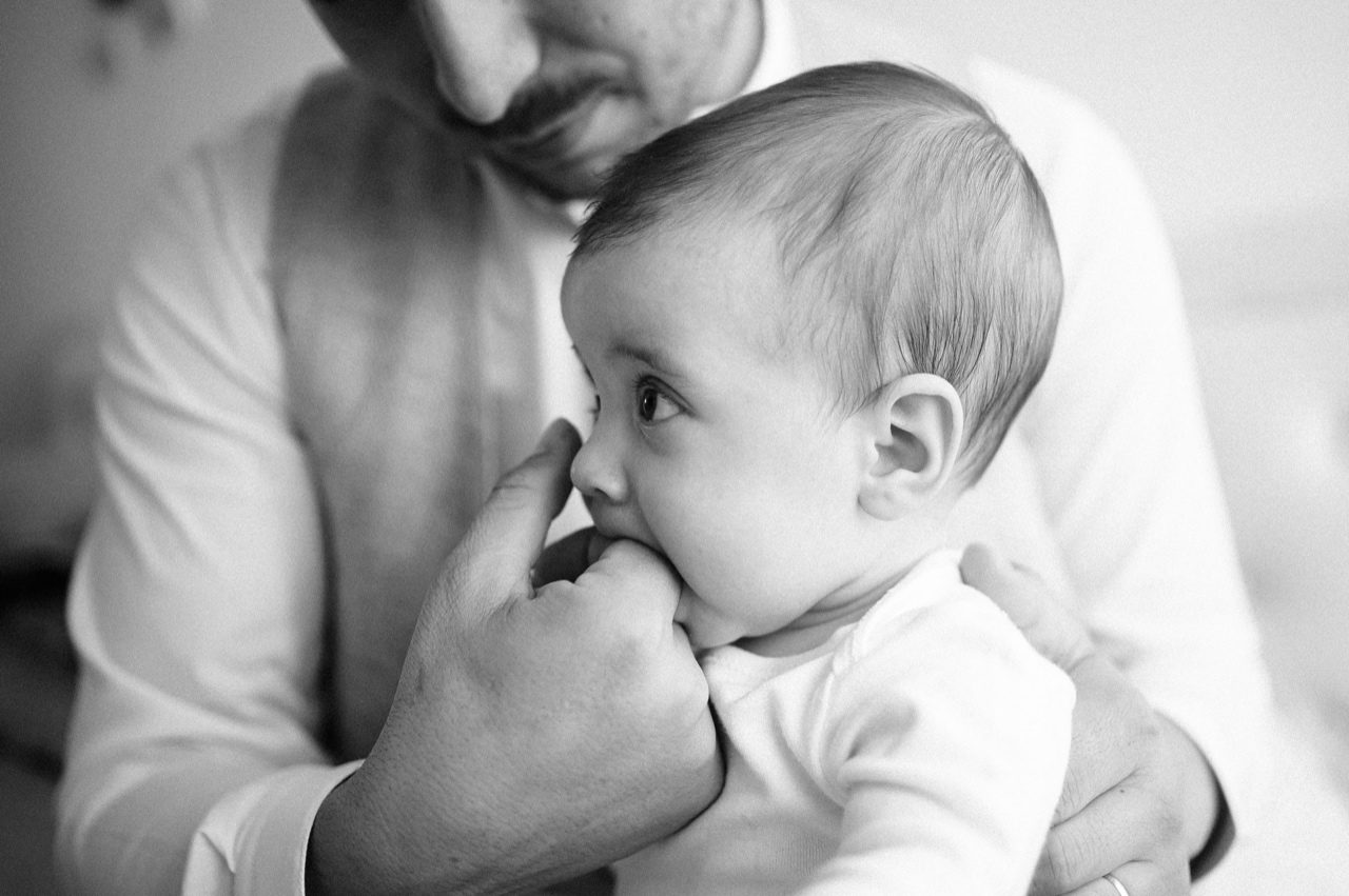 Preparativi battesimo Roma — bambino morde affettuosamente il dito del papà, primo piano in bianco e nero
