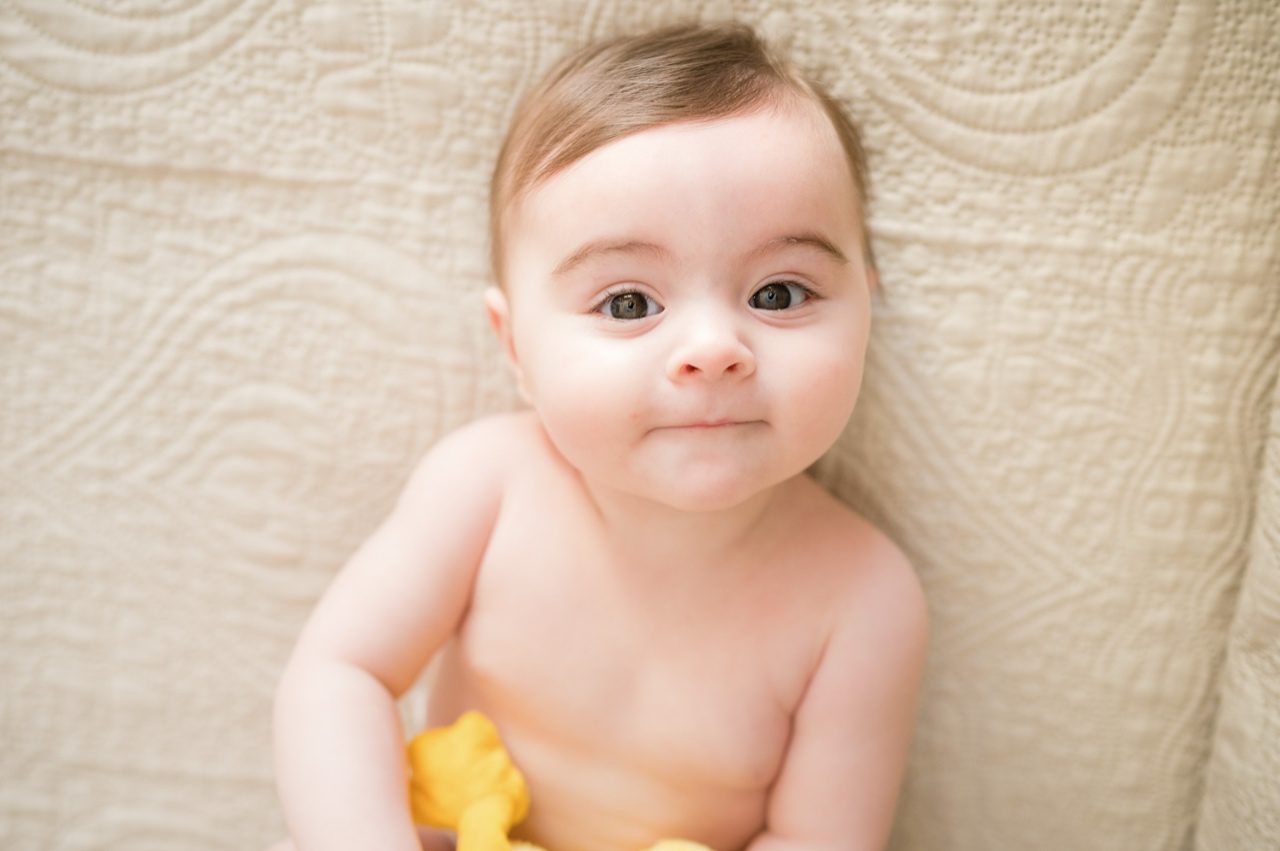 Preparativi battesimo Roma — ritratto della bambina su coperta beige nella cameretta